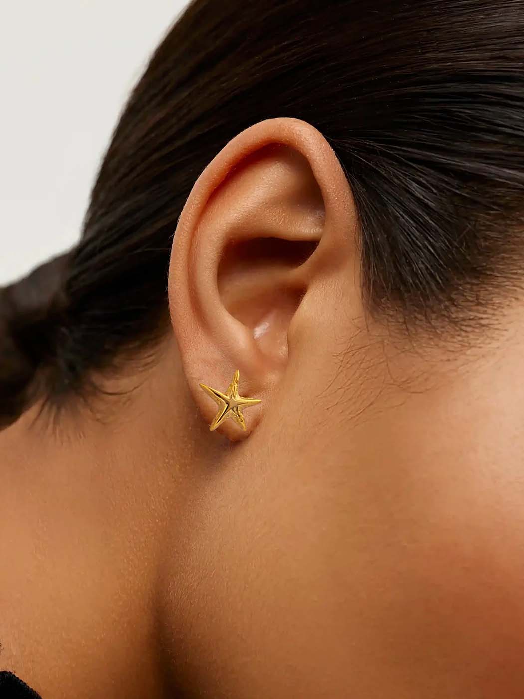 Gold starfish-shaped earring worn by a person with a neutral background