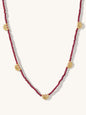 A beaded necklace featuring garnet round beads and five gold-toned circular sunburst charms spaced along the strand, displayed against a light cream background.
